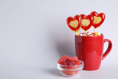 Photo of Delicious heart shaped lollipops, dragees and jelly candies on light background