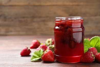 Photo of Delicious pickled strawberry jam and fresh berries on wooden table. Space for text