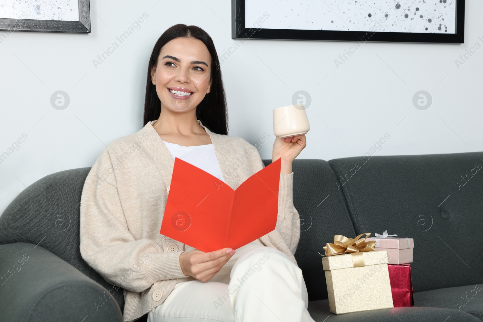 Photo of Happy woman reading greeting card while drinking coffee on sofa in living room