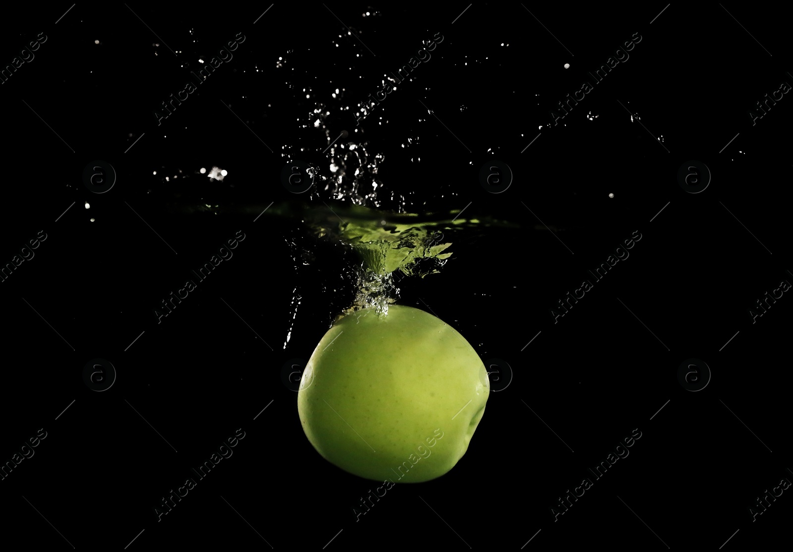 Photo of Green apple falling down into clear water against black background
