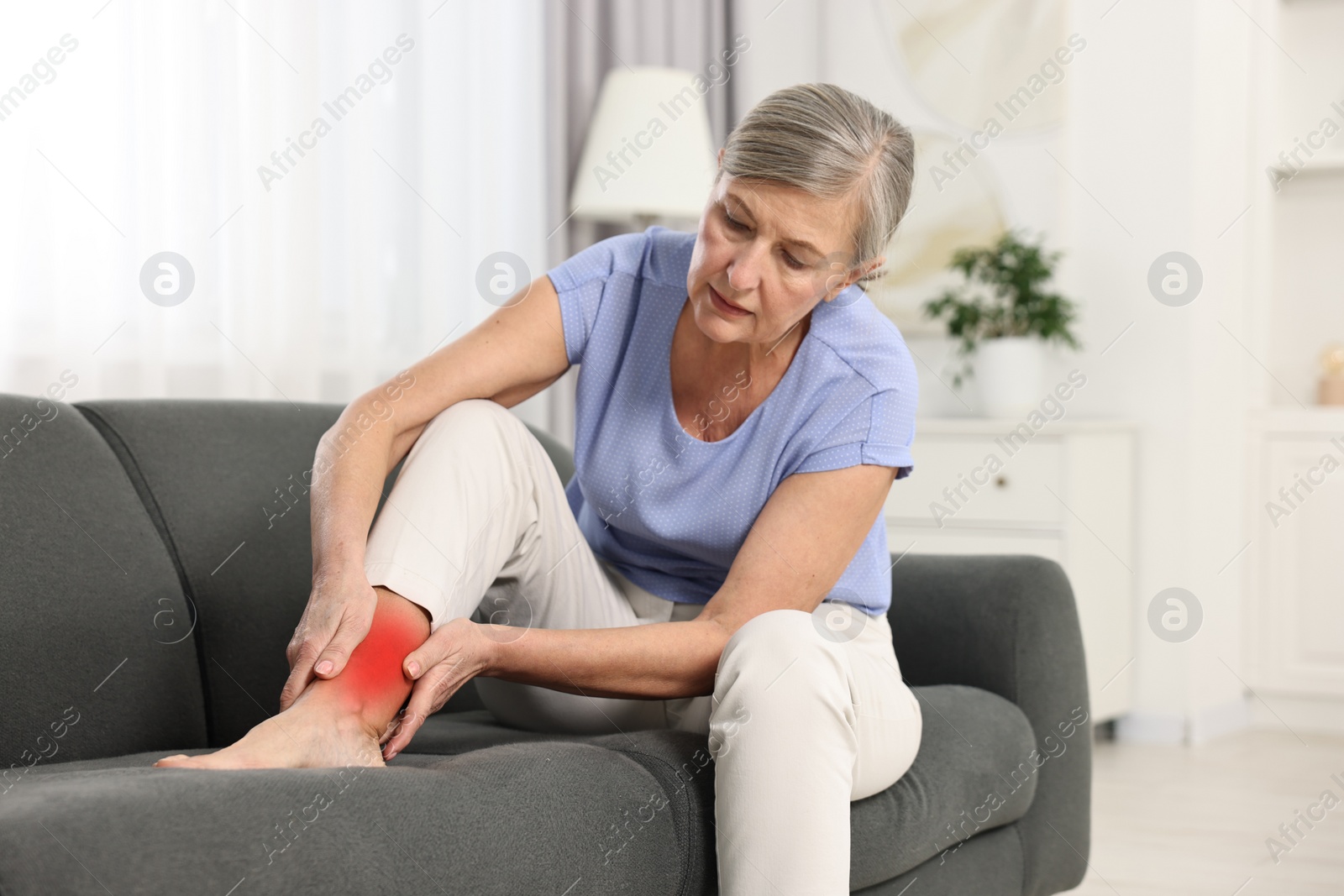 Image of Senior woman suffering from pain in ankle on sofa indoors