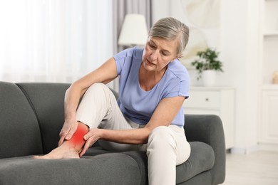 Senior woman suffering from pain in ankle on sofa indoors