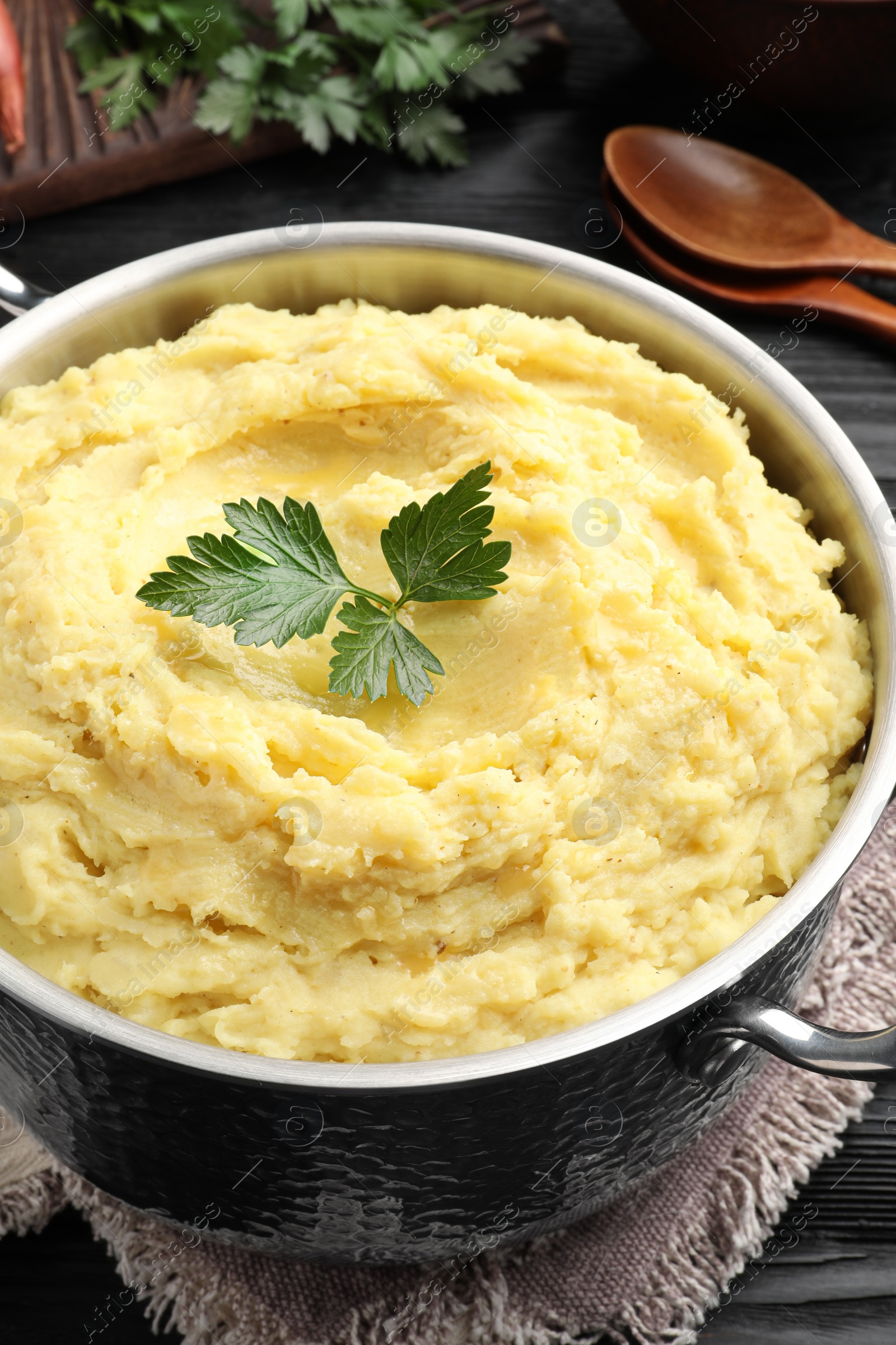 Photo of Pot of tasty mashed potatoes with parsley on black wooden table