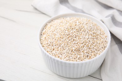 Photo of Dry barley groats in bowl on white wooden table, closeup. Space for text