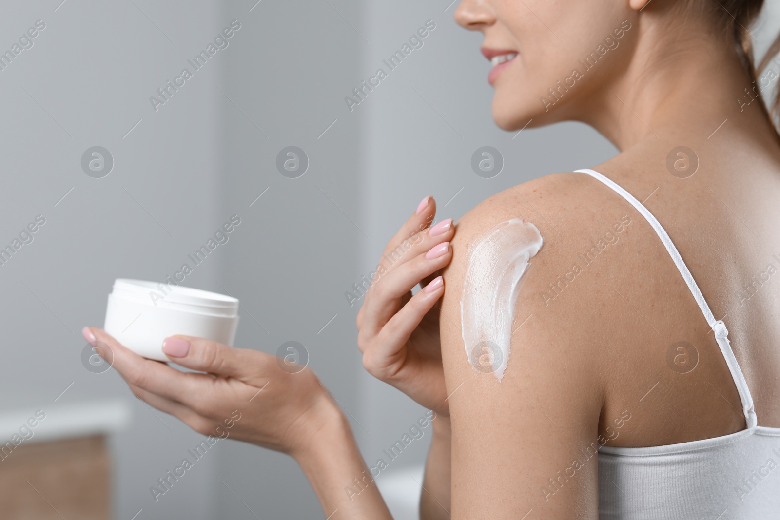 Photo of Woman applying body cream onto shoulder indoors, closeup