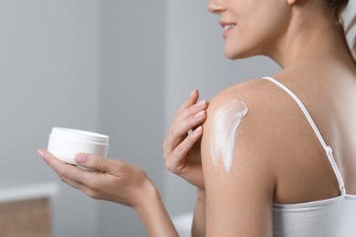 Woman applying body cream onto shoulder indoors, closeup