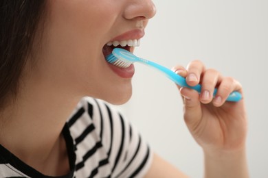 Woman brushing her teeth with plastic toothbrush on white background, closeup
