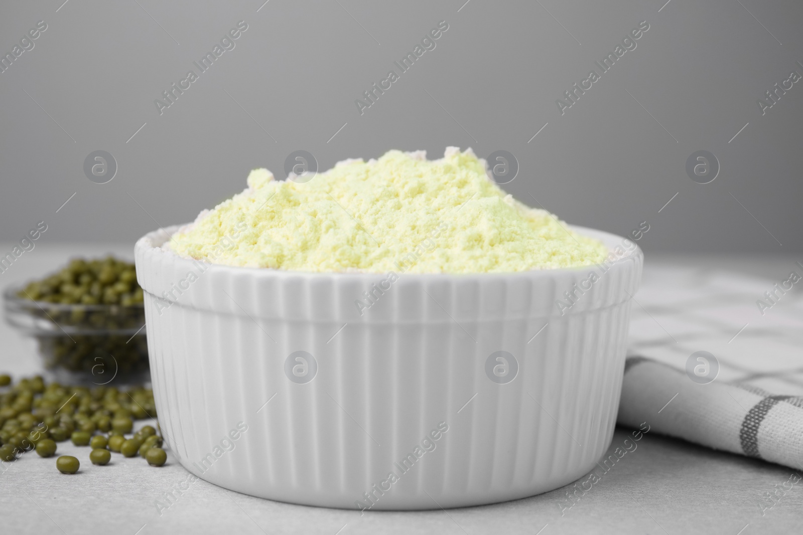 Photo of Mung bean flour in bowl and seeds on white table, closeup