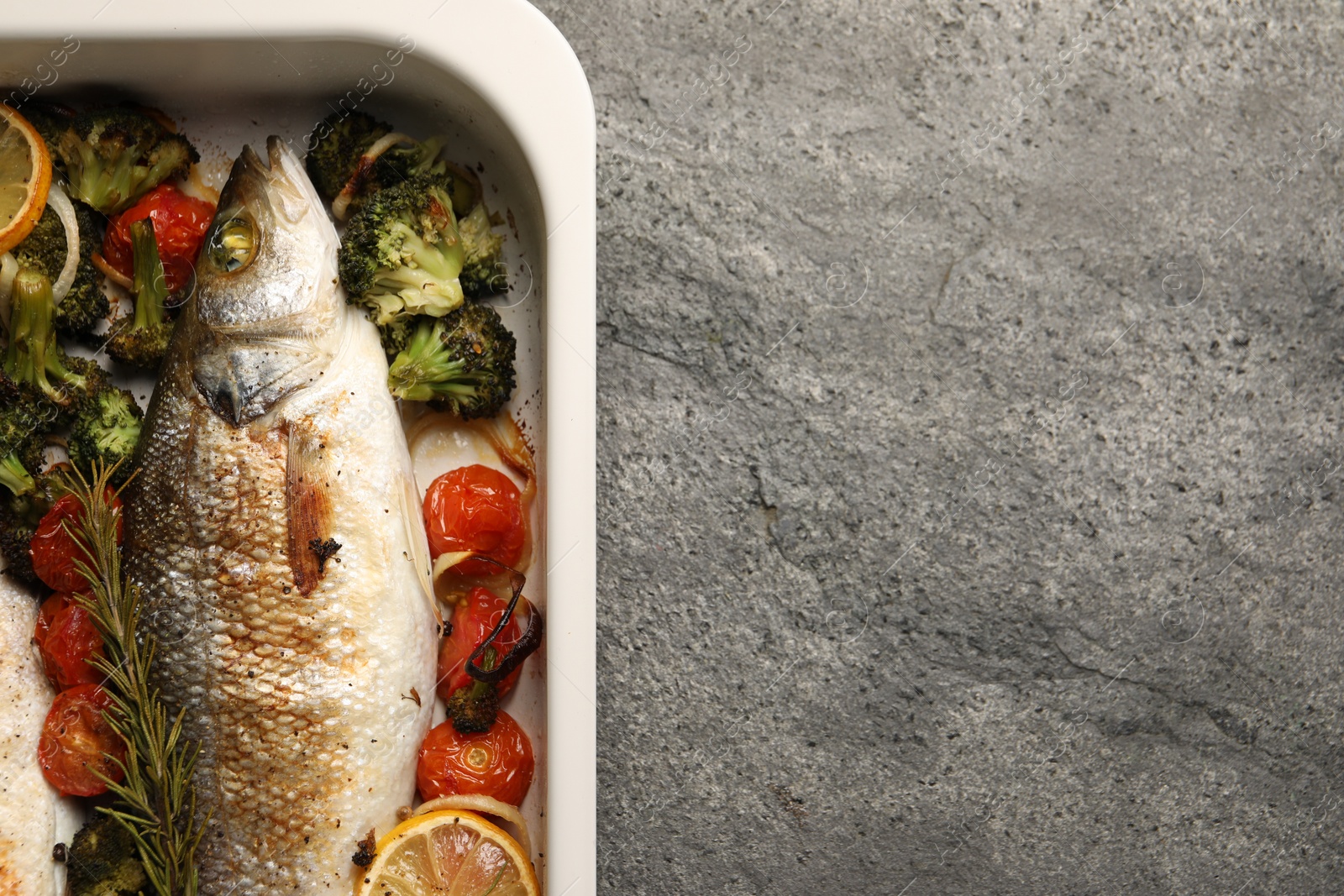 Photo of Delicious fish with vegetables and lemon in baking dish on grey textured table, top view. Space for text