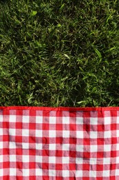 Photo of Checkered picnic tablecloth on fresh green grass, top view. Space for text