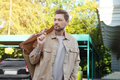 Photo of Attractive serious man holding garment cover with clothes outdoors. Dry cleaning service