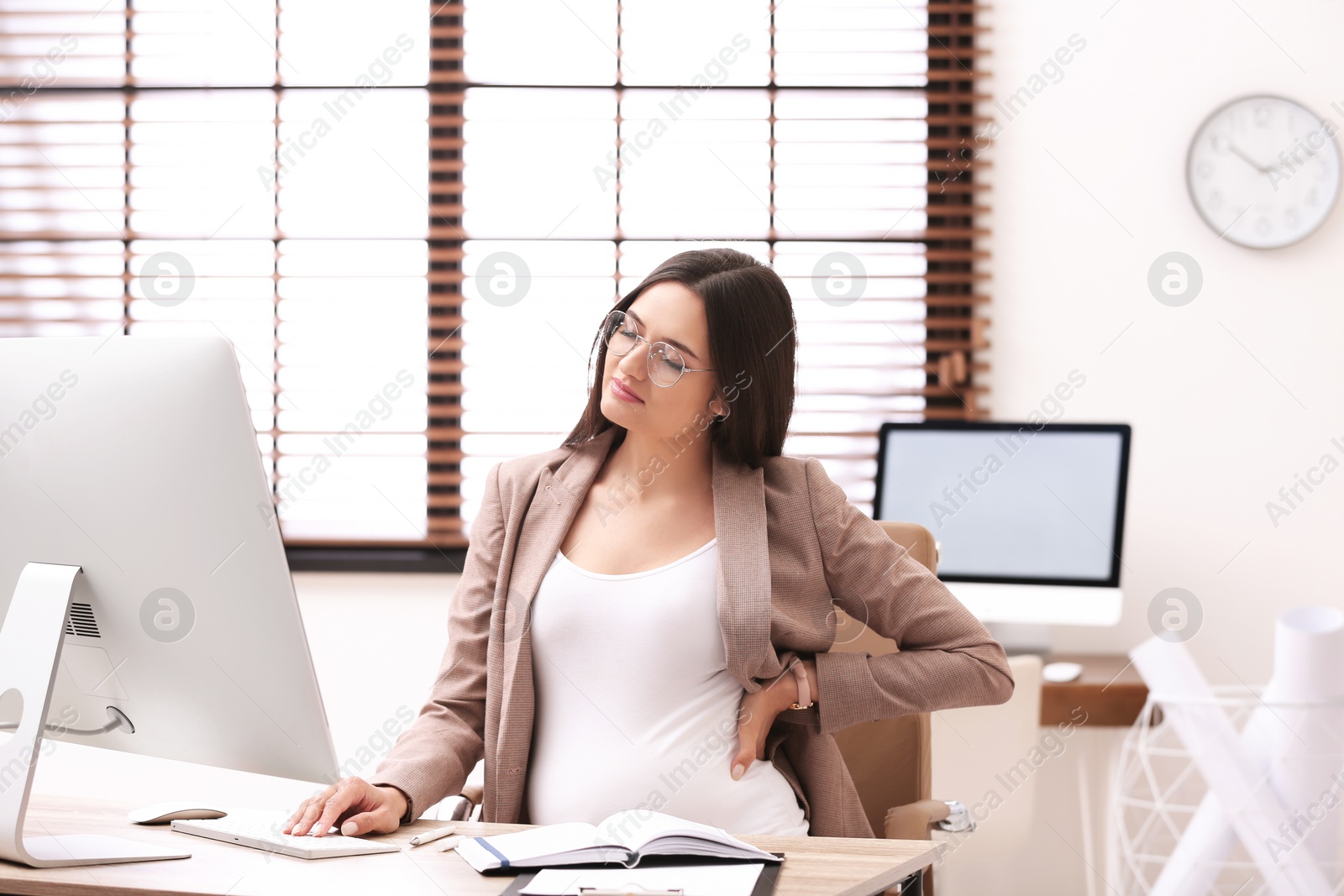 Photo of Young pregnant woman suffering from pain while working in office