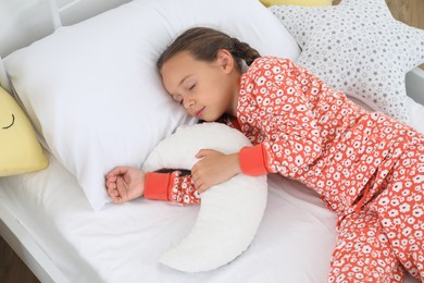 Photo of Cute girl in pajamas sleeping with moon shaped pillow at home