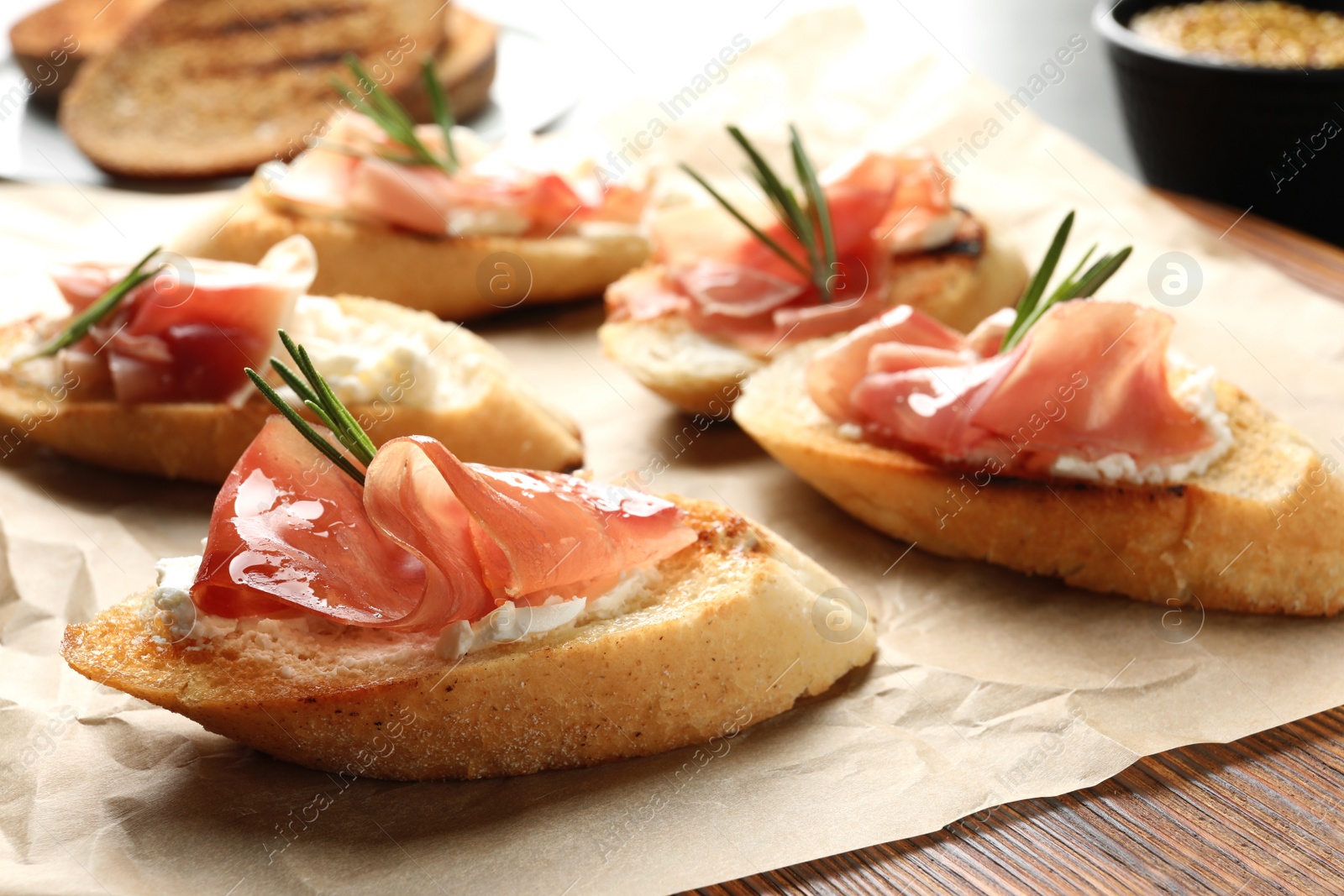 Photo of Tasty bruschettas with prosciutto and cream cheese on parchment, closeup