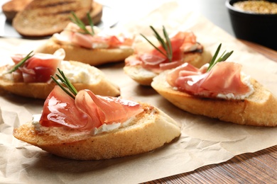 Photo of Tasty bruschettas with prosciutto and cream cheese on parchment, closeup