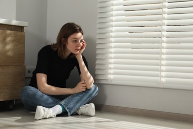 Sad young woman sitting on floor indoors, space for text