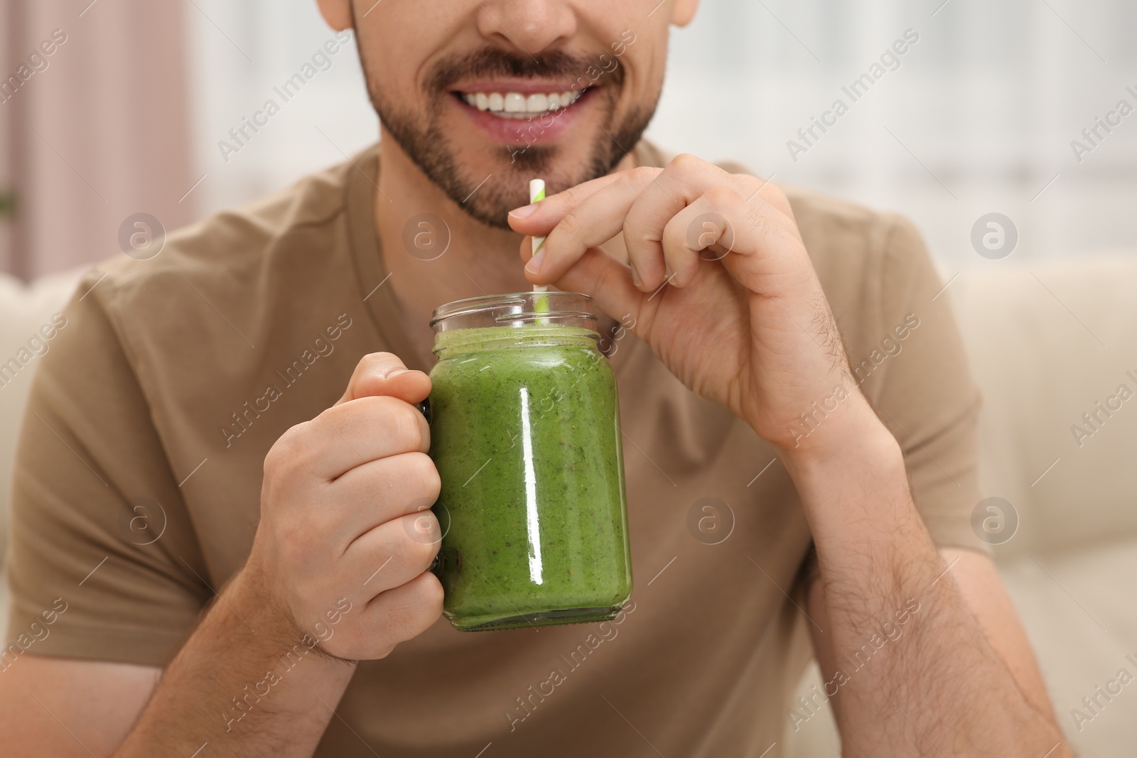 Photo of Happy man drinking delicious fresh smoothie indoors, closeup