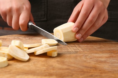 Photo of Woman cutting delicious fresh ripe parsnip at wooden board, closeup