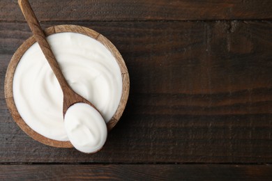 Delicious natural yogurt in bowl and spoon on wooden table, top view. Space for text