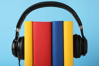 Photo of Books and modern headphones on light blue background, closeup