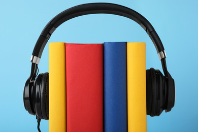 Books and modern headphones on light blue background, closeup