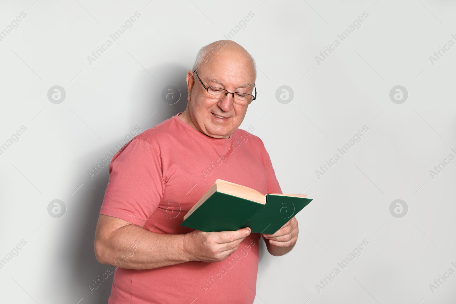 Photo of Portrait of senior man with glasses reading book on light background. Space for text