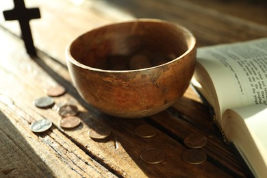 Donate and give concept. Bowl with coins, cross and Bible on wooden table in sunlights, selective focus