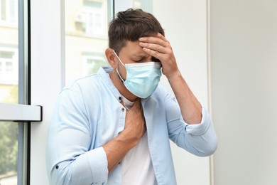 Photo of Man in medical mask suffering from pain during breathing near window