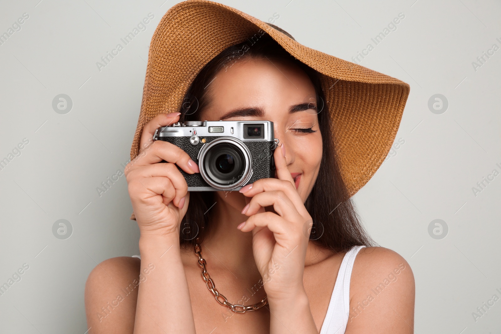 Photo of Beautiful young woman with straw hat and camera on light grey background. Stylish headdress