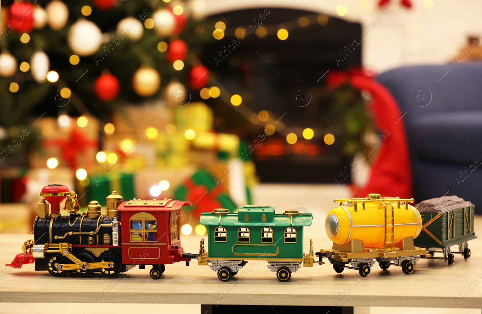 Photo of Beautiful toy train on wooden table against blurred festive lights. Christmas celebration