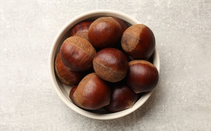 Roasted edible sweet chestnuts in bowl on light grey table, top view