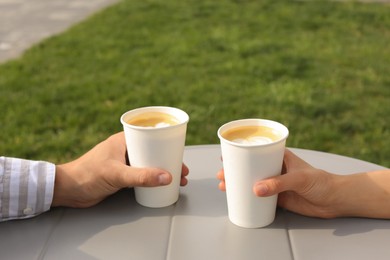 Photo of Coffee to go. Couple with paper cups at grey table outdoors, closeup