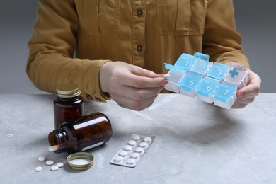 Photo of Woman putting pill into weekly organizer at grey marble table, closeup