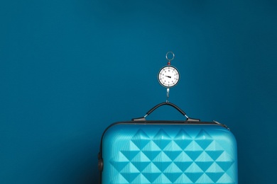 Photo of Modern suitcase and hanging scales against color background, space for text