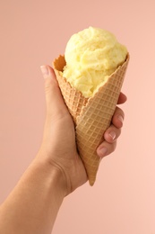 Woman holding yellow ice cream in wafer cone on pink background, closeup