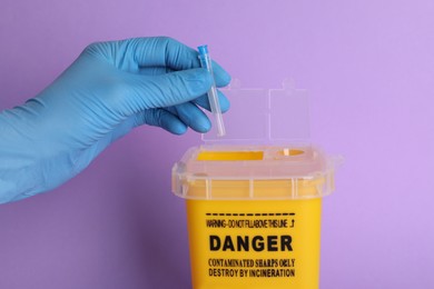 Photo of Doctor throwing used syringe needle into sharps container on violet background, closeup