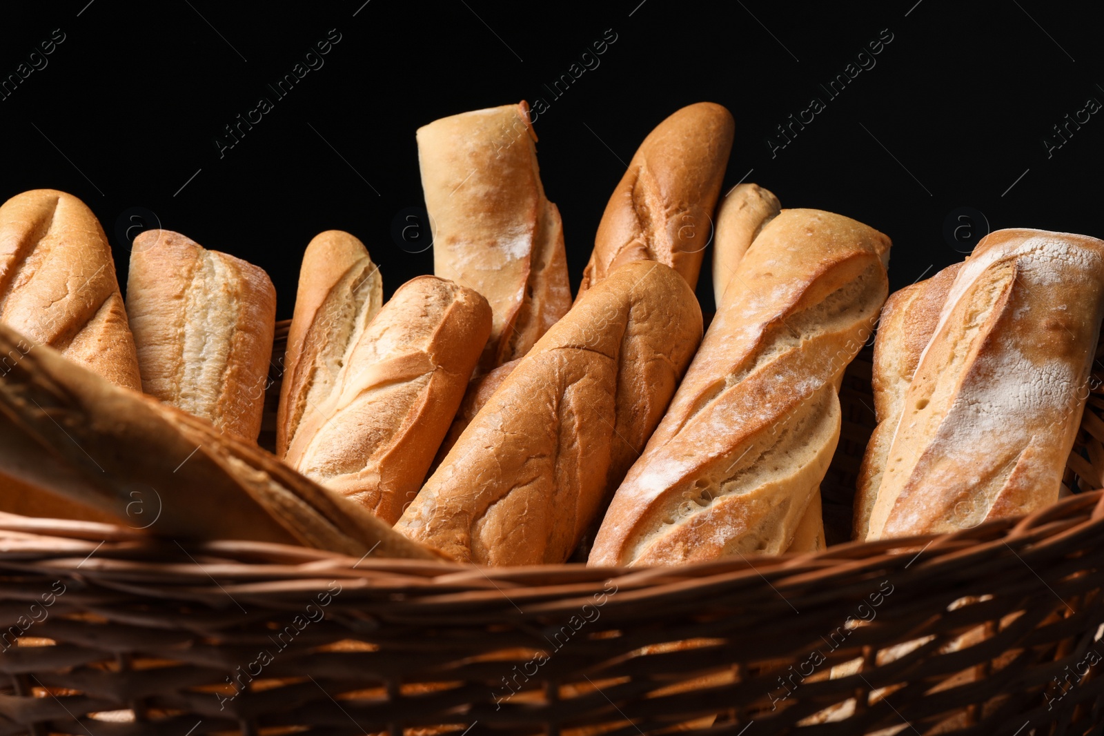 Photo of Fresh tasty baguettes in basket against black background, closeup