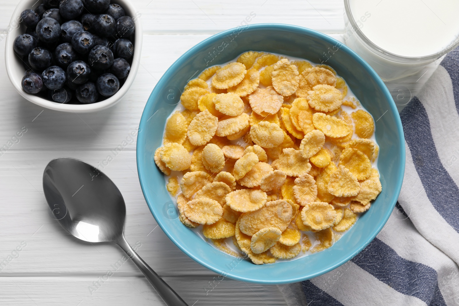 Photo of Bowl of tasty corn flakes and blueberries served for breakfast on white wooden table, flat lay