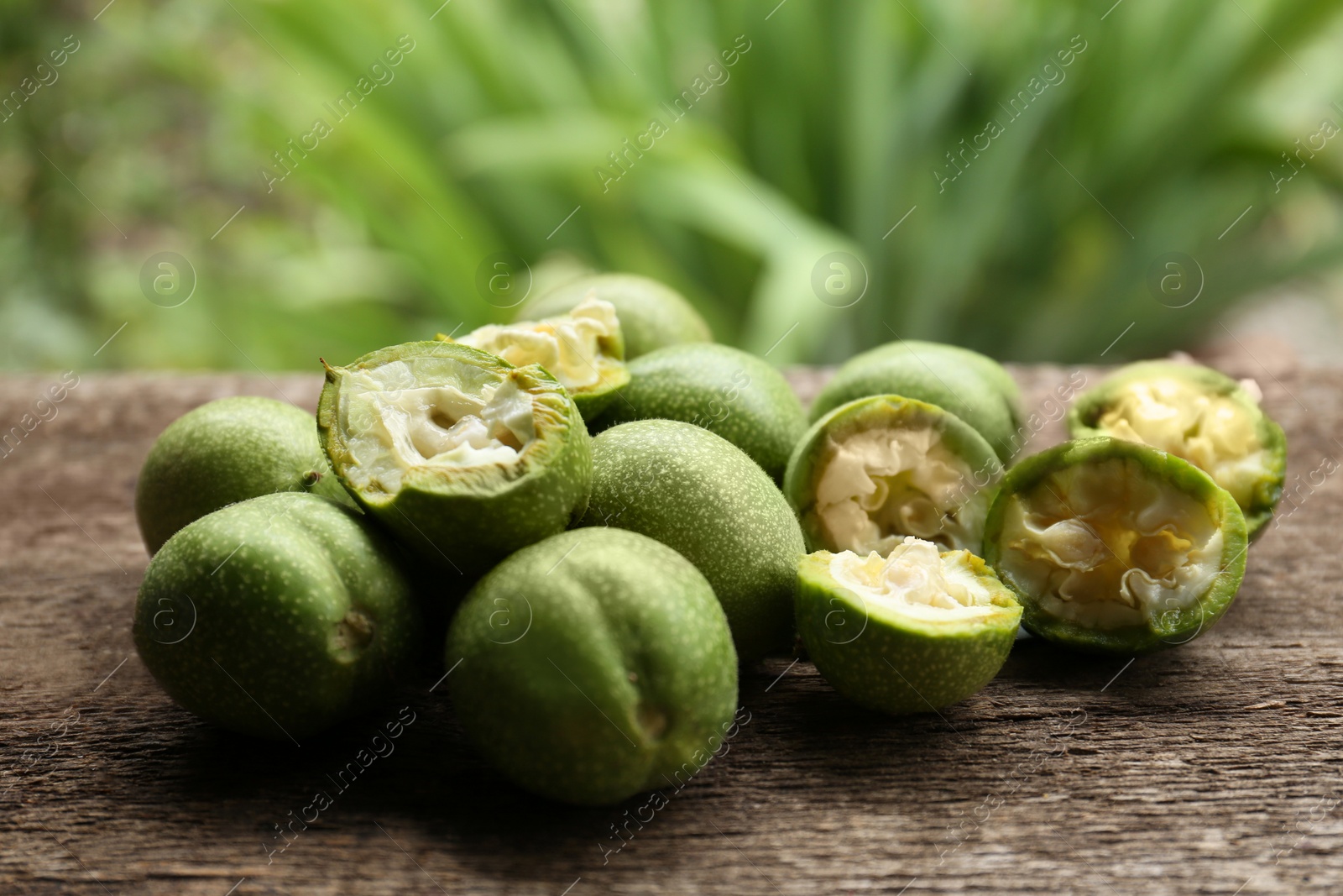 Photo of Whole and broken green walnuts on wooden table against blurred background, closeup