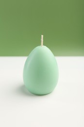 Photo of Green egg shaped candle on white table. Easter decor
