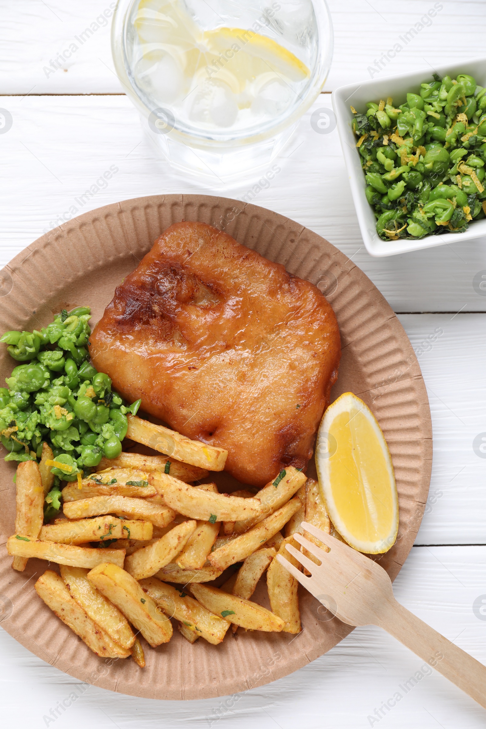 Photo of Tasty fish, chips, peas and lemon on white wooden table, top view