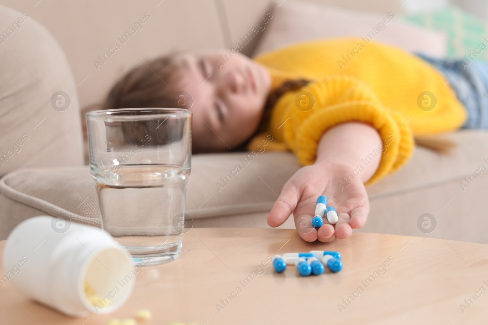 Photo of Unconscious little child with pills on sofa at home. Danger of medicament intoxication