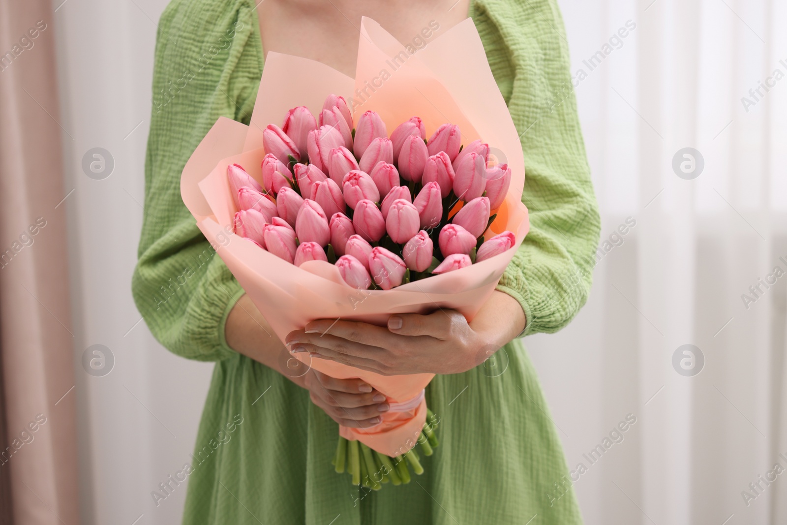 Photo of Woman holding bouquet of pink tulips indoors, closeup