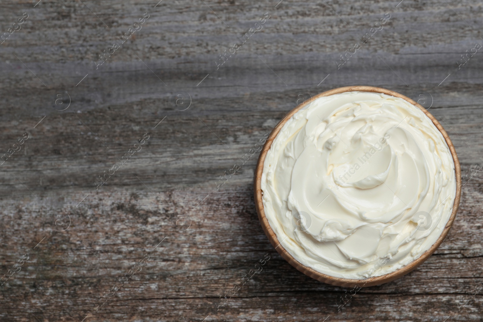 Photo of Bowl of tasty cream cheese on wooden table, top view. Space for text