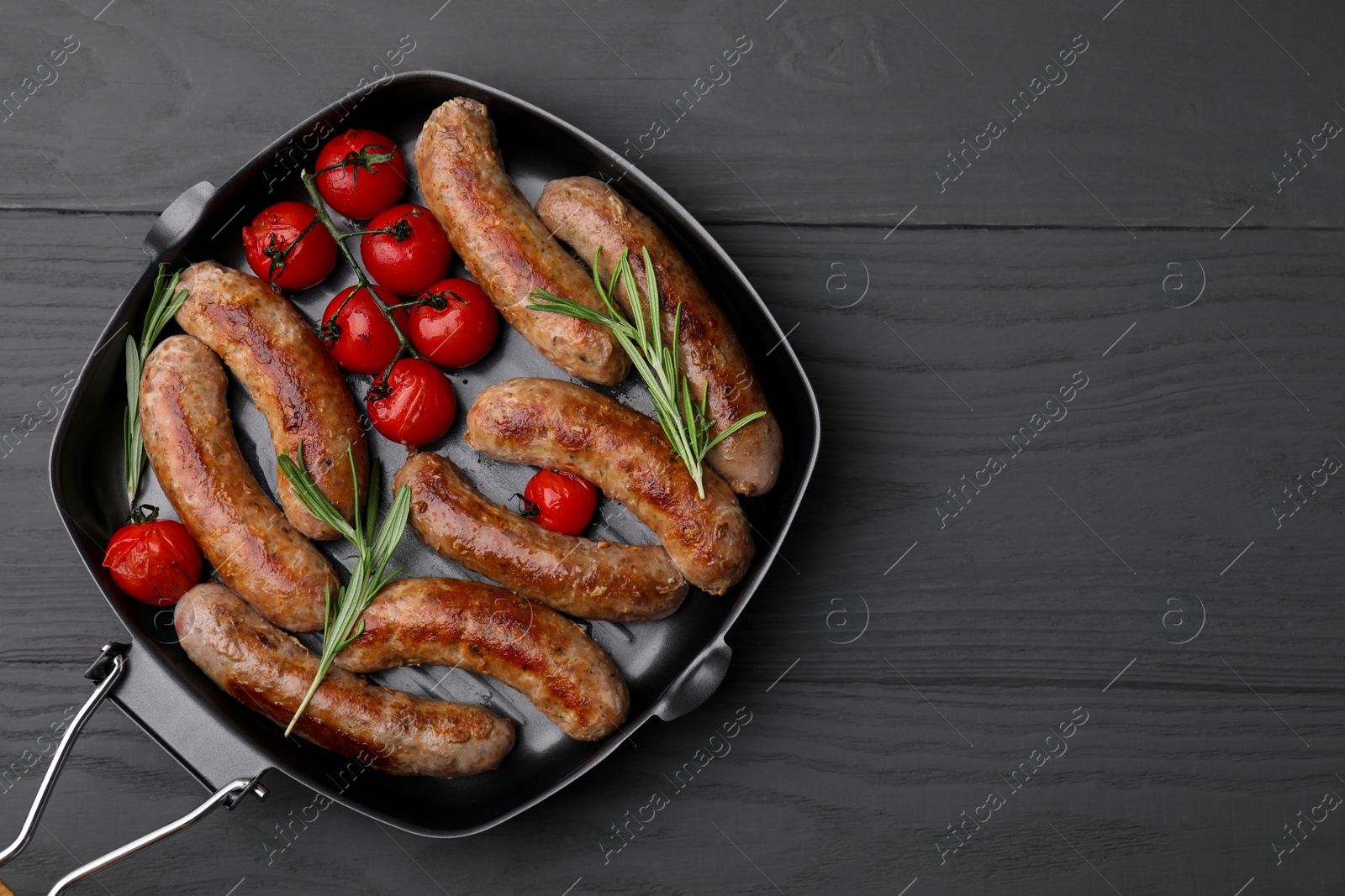 Photo of Grill pan with tasty homemade sausages, rosemary and tomatoes on grey wooden table, top view. Space for text