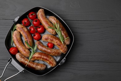 Photo of Grill pan with tasty homemade sausages, rosemary and tomatoes on grey wooden table, top view. Space for text