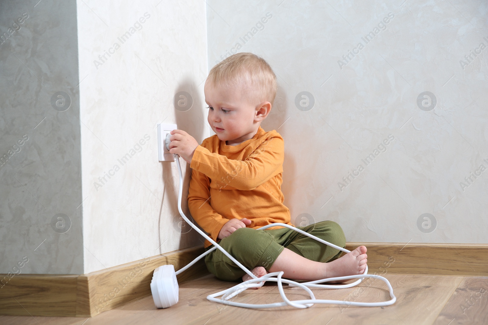 Photo of Little child playing with electrical socket and power strip plug at home. Dangerous situation