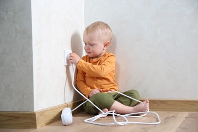 Photo of Little child playing with electrical socket and power strip plug at home. Dangerous situation