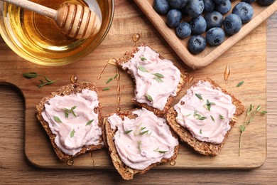 Photo of Tasty sandwiches with cream cheese, honey and thyme on wooden table, flat lay