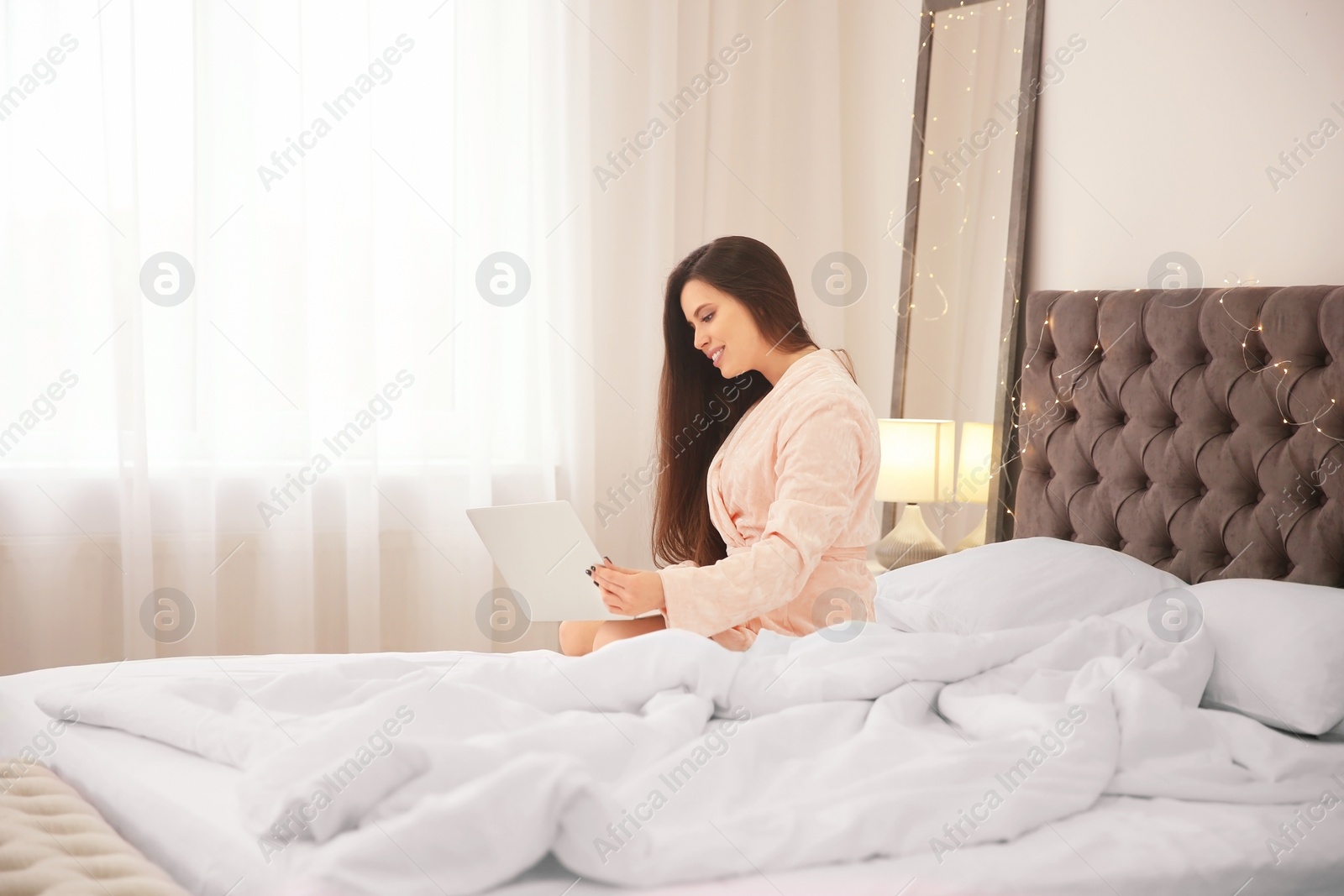 Photo of Young woman using laptop on bed in hotel room